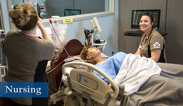 two nursing students take care of a manikin in a hospital bed