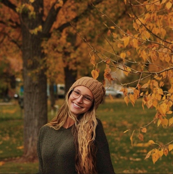 young woman in wool hat with long blond hair standing in beautiful golden autumn foliage