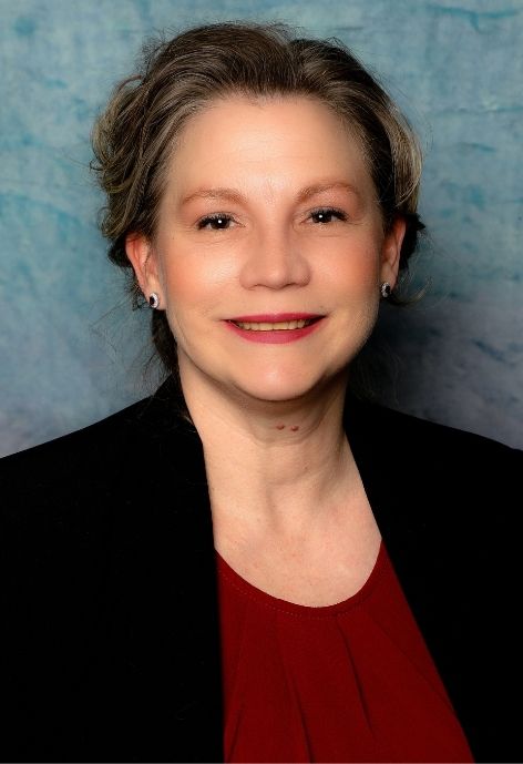 jennifer stephens in red blouse with black suit jacket in front of blue photo backdrop