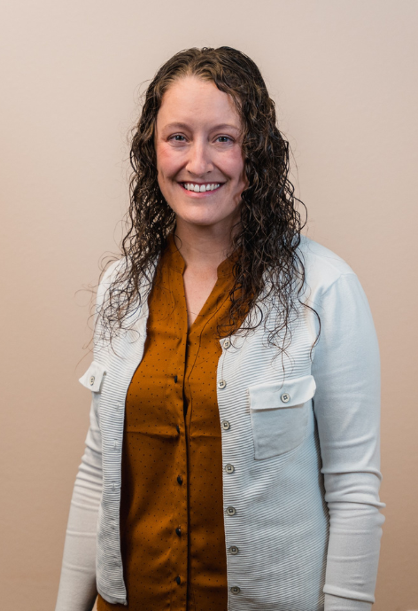 lisa western wearing an rust colored shirt with a cream colored jacket standing in front of a cream back drop