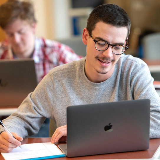 student on a computer taking notes