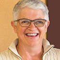smiling woman with short cropped white/grey hair, glasses, in cream sweater