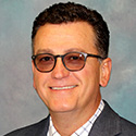 man with curly short dark hair and shaded glasses in business attire