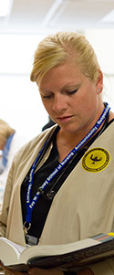 young woman with blonde hair in nursing uniform studying textbook