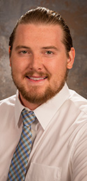 Young man dressed professionally with hair slicked back, beard and mustache