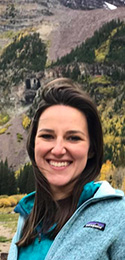 woman in aqua jacket and wind-blown dark hair in mountains