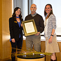 Three individuals pose with award plaque