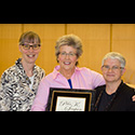 Three women pose with award plaque.