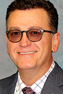 Man with shaded classes, short dark hair, suit and tie