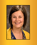 Smiling woman with short brown hair, wearing bright gold sweater