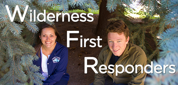a young woman and a young man crouch beneath a blue spruce tree, framed by the greenery