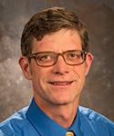 portrait of man with brown hair, glasses and a bright blue shirt and tie