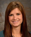 young woman with dark brown hair in professional dark green suit and necklace