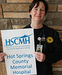 Laura Williams standing in front of a brick wall holding the hospital sign