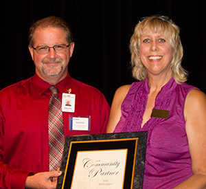 man in red shirt and glasses accepts plaque from woman in purple shirt and blonde hair