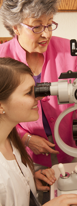 Pink-clad woman guides student with eye observation equipment