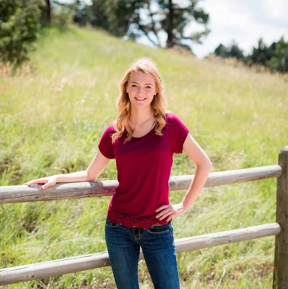 young woman leaning on a wooden fence in a grassy field