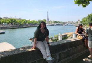 julia sharpes sitting outside on a rock wall with the eiffel tower in the back