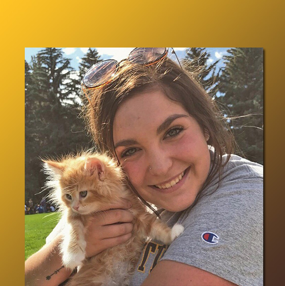 close-up of young woman hugging a kitten outside in a grassy field