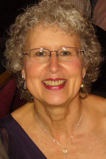 woman with curly hair highlighted with grey, in glasses, earrings, and a lovely smile