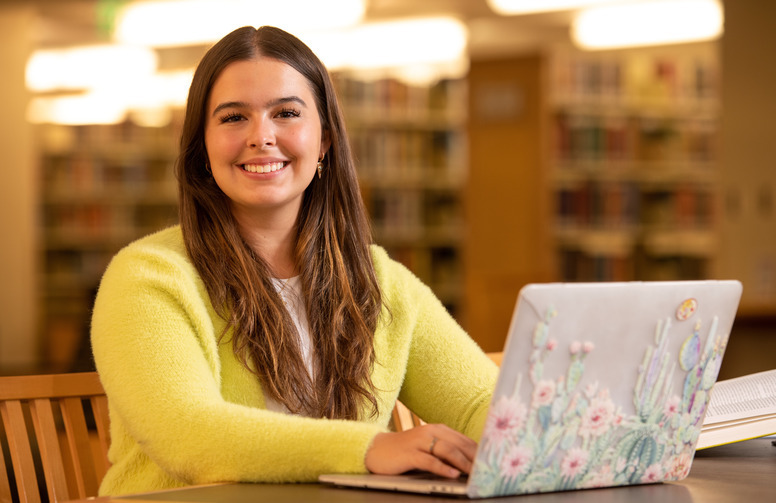 woman poses with her laptop in the library.