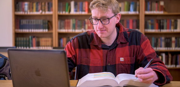 A UW student has a textbook and laptop in front of them as they pursue a UW online degree.