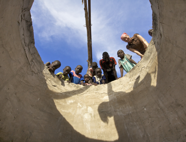 A Peace Corps volunteer and children looking down to the bottom of a well