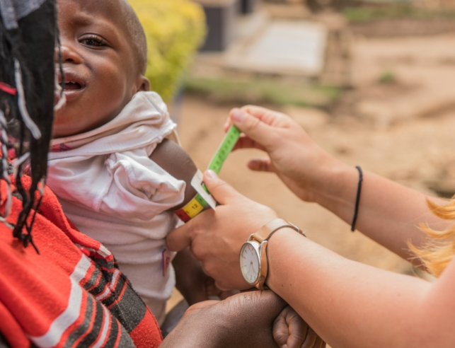 An infant in his mother's arms getting a physical from a Peace Corps volunteer