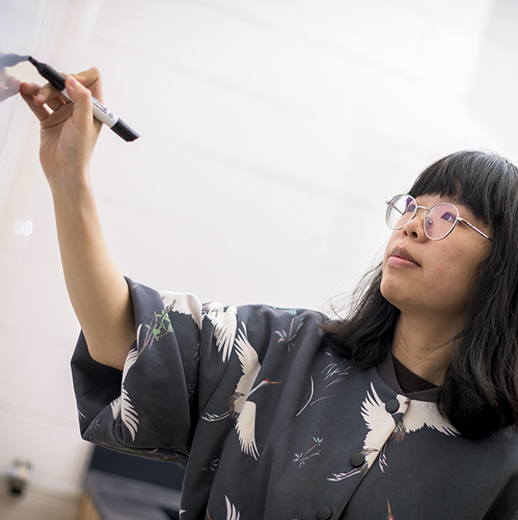 student wearing glasses writing on a white board