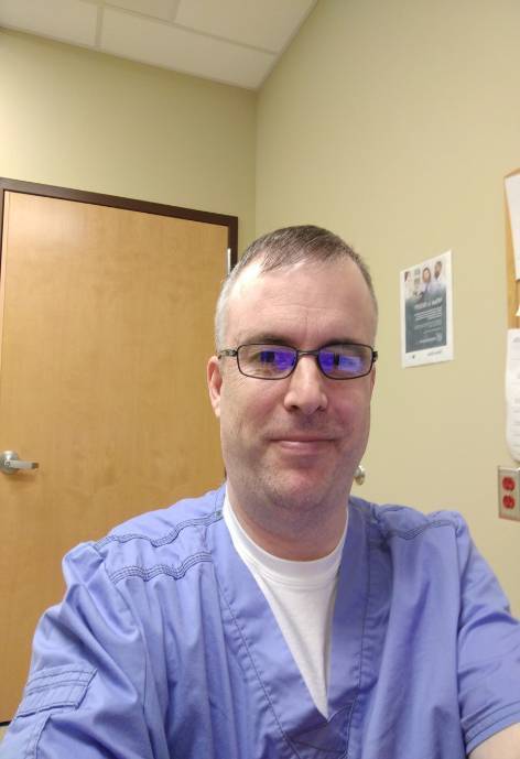 Man wearing glasses and blue scrubs