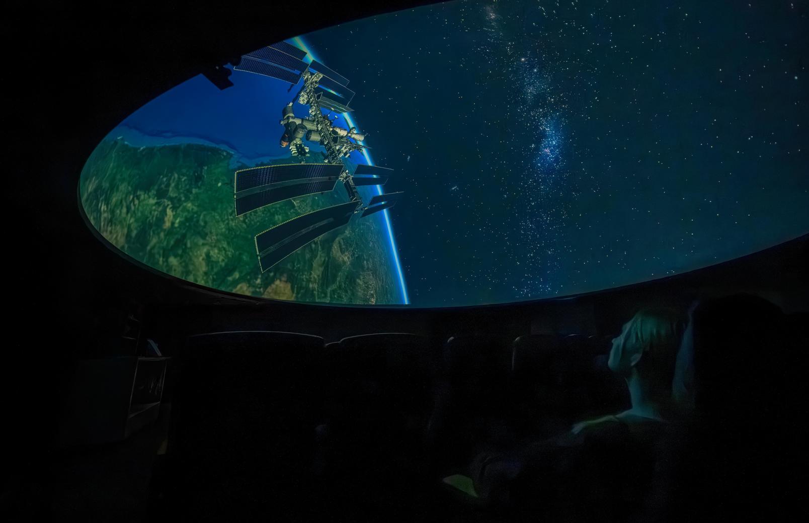A person sits behind a computer at the UW planetarium and observes planets and stars on the expansive dome screen.