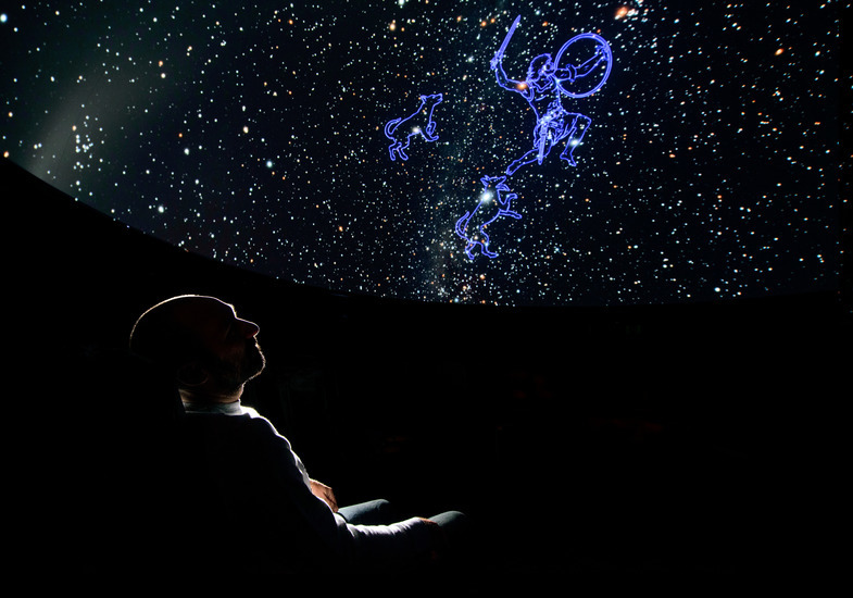 A person sits in the UW planetarium dome and observes constellations projected overhead.