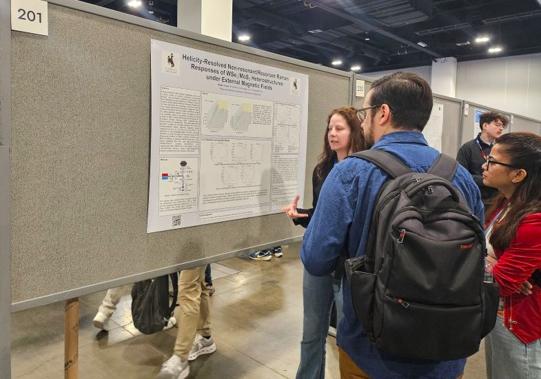 person in background explaining scientific poster on a divider to a small crowd