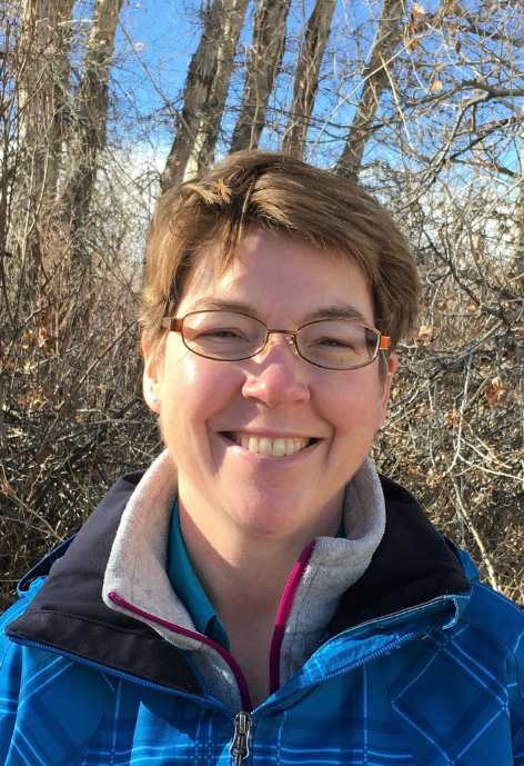 Smiling woman wearing blue plaid jacket outside with trees