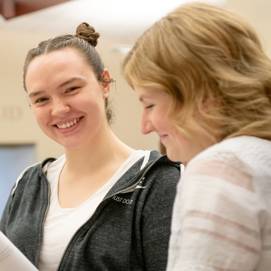 A student smiles at the camera while speaking with a staff member