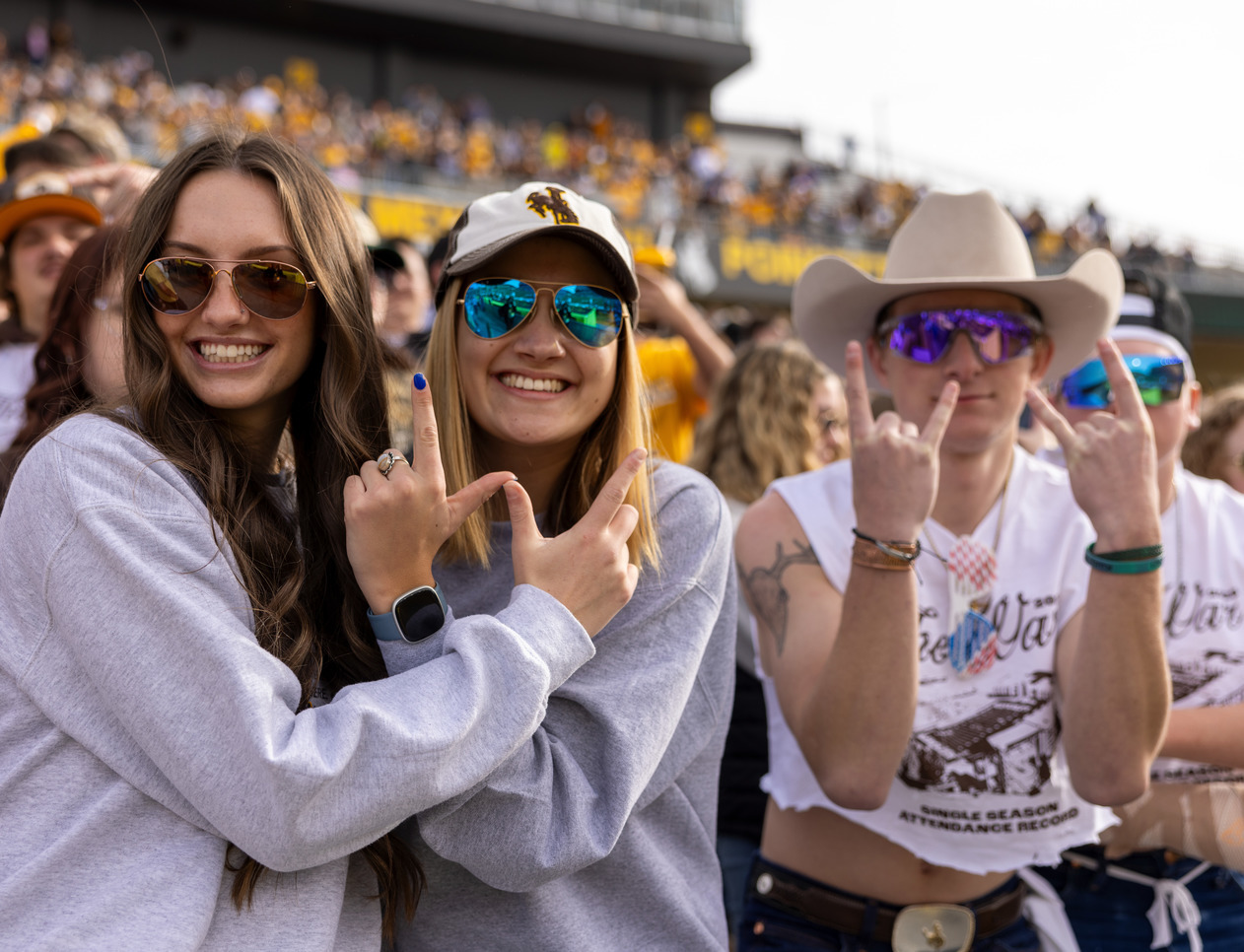 Students making a "w" signal with their hands and posing for the camera at a UW Cowboys football game.