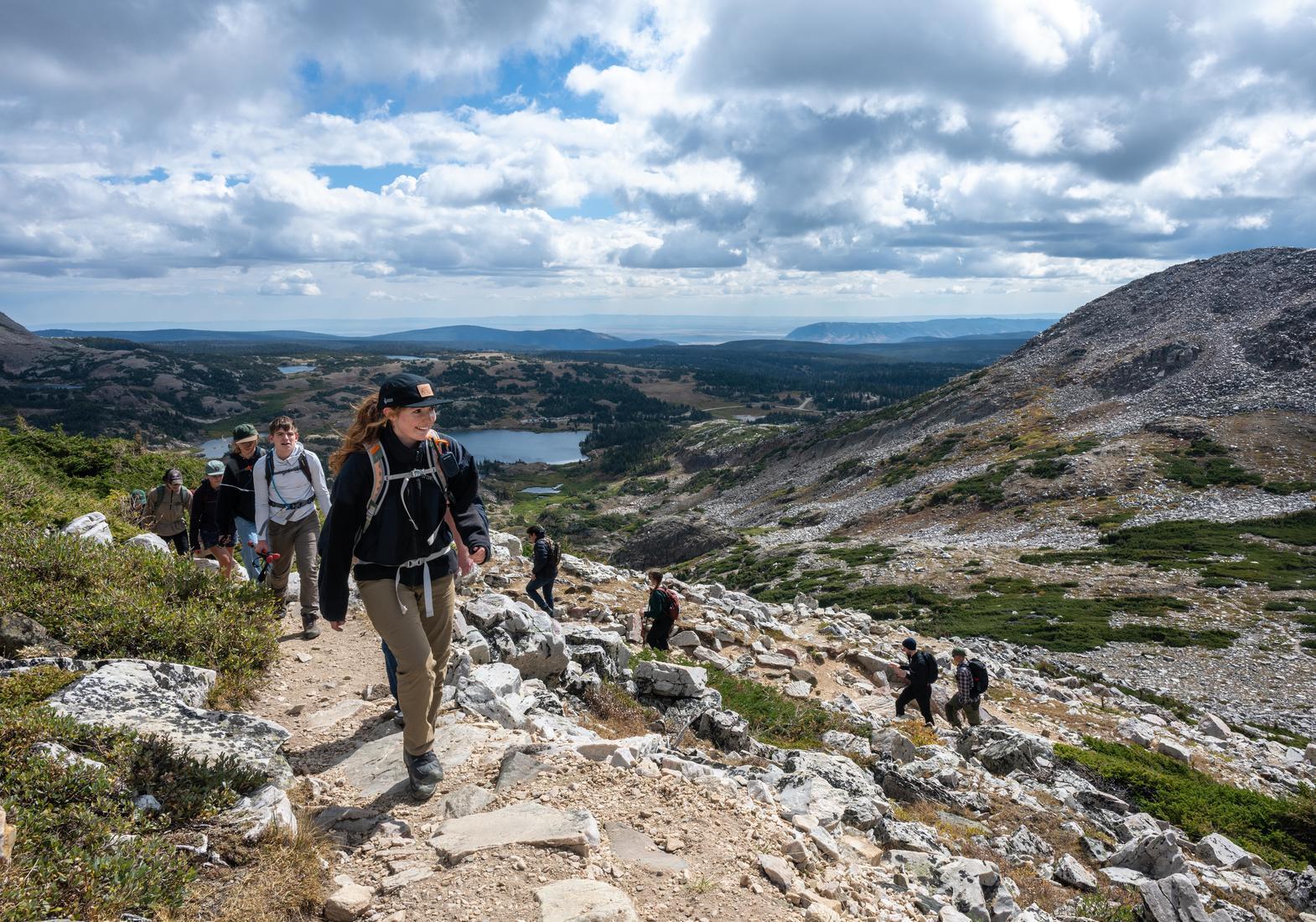 Students hike up a trail with a vast view of the Snowy Range in the background.