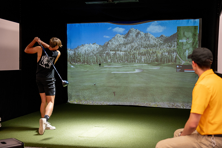 A student uses the golf simulator in Half Acre.