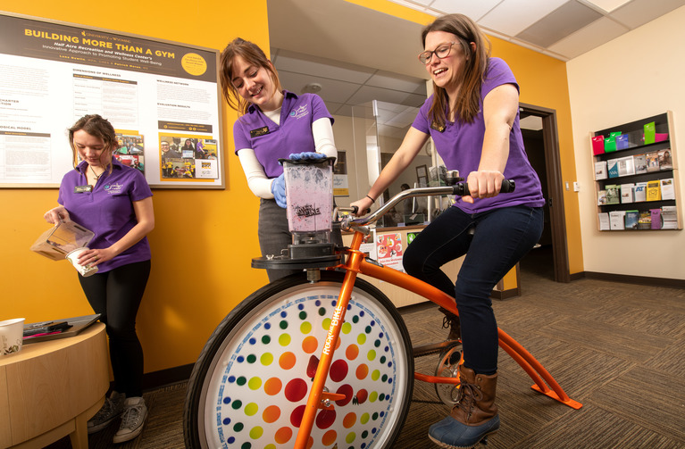 Student staff use the smoothie bike in the Wellness Center
