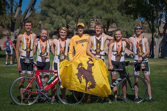 The Triathlon team poses with a yellow Wyoming Cowboys flag