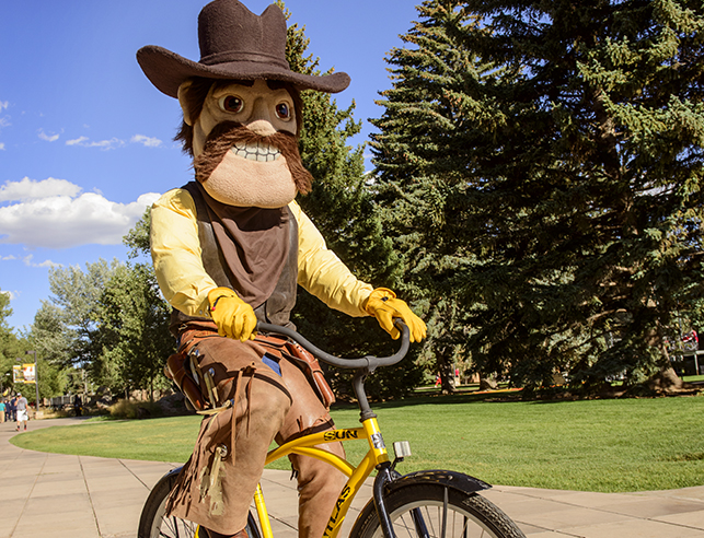 Pistol Pete rides a yellow bike in Prexy's Pasture