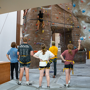 Students watch as a climber acsends the Climbing Wall in Half Acre
