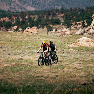 Two people mountain bike in an open field