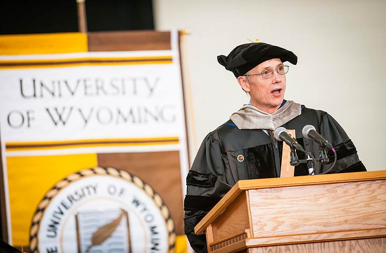a person wearing commencement regalia is speaking at a UW commencement ceremony