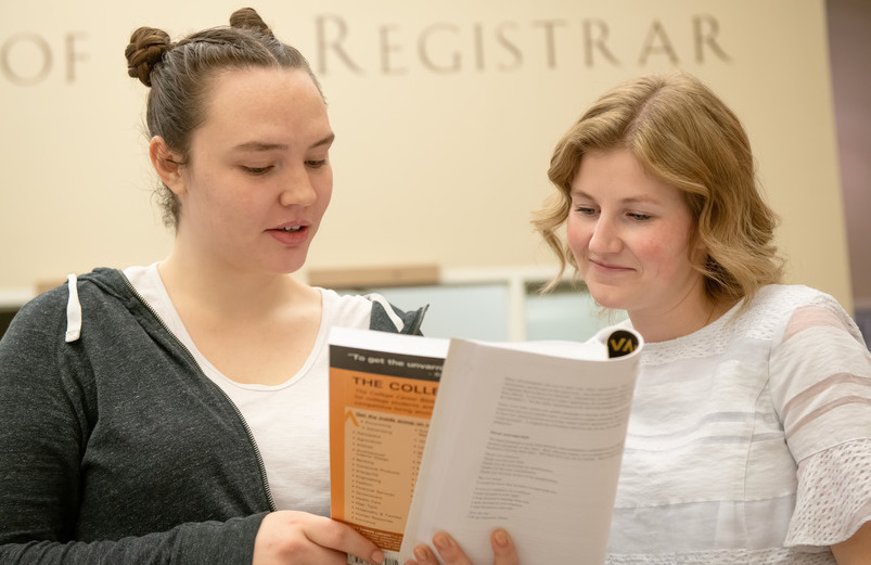 Student and advisor reviewing college catalog in front of the Office of the Registrar in Knight Hall.