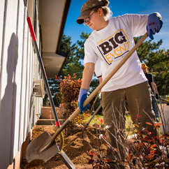 Student wearing a Big Event t-shirt using a shovel to replant some flowers at a volunteer event.