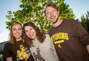 Three students smiling for a picture with green tress behind them.
