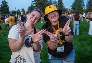 Two students at an outdoor event holding up W finger sign.