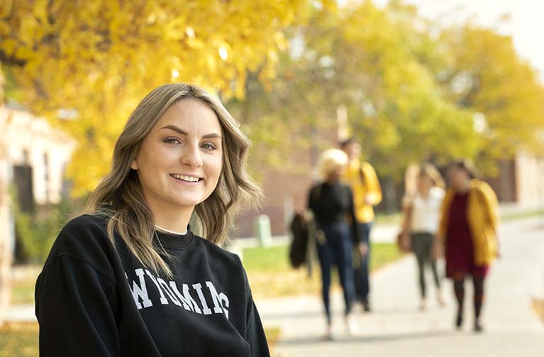 a smiling student wearing a UW sweatshirt outside in the fall