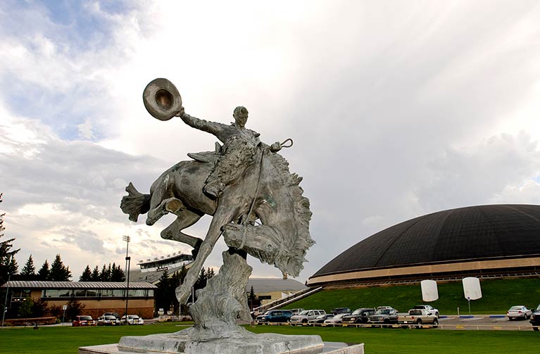 a statue of a rider on a bucking horse that is in front of the UW Arena Auditorium